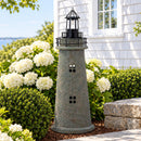 Weathered brown and green lighthouse statue displayed on a brick garden wall surrounded by blue hydrangeas, pink flowers, and greenery in a landscaped front yard.