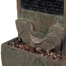Close-up view of the curved water spillway flowing into a basin filled with decorative rocks on an outdoor wall fountain.