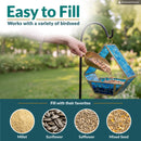 Modern Mosaic Fly-Through Bird Feeder in blue shown being filled with birdseed in a garden. Open design makes filling easy and works with millet, sunflower, safflower, and mixed seed.