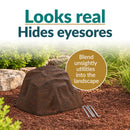 Dark brown artificial landscape rock with realistic stone texture displayed in a mulched garden with decorative stones and greenery, designed to conceal outdoor utilities while blending naturally into the landscape.