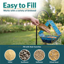Modern Mosaic Fly-Through Bird Feeder in blue shown being filled with birdseed in a garden. Open design makes filling easy and works with millet, sunflower, safflower, and mixed seed.