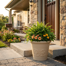 Tan decorative planter filled with lush greenery and colorful flowers, displayed on a front porch beside a stone entryway.