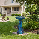 Crackled Glass Mosaic Bird Bath in deep ocean swirl shown outdoors in a landscaped backyard, featuring a shimmering blue and turquoise crackled glass bowl and pedestal.