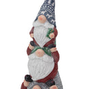 Close-up view of a stacked Christmas gnome statue featuring three gnomes with white beards, patterned hats, and red and green details on a white background.
