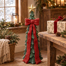 Green Christmas tree sculpture with a red bow and gold star displayed beside a rustic table with a wrapped gift and holiday greenery.