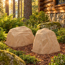 Two tan artificial landscape rocks with realistic sandstone textures displayed side by side in a rustic woodland garden beside a log cabin, surrounded by ferns, moss-covered stones, and mulch in warm afternoon sunlight.