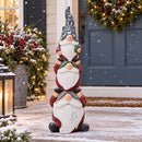 Stacked Christmas gnome statue displayed outdoors in a snowy setting beside a decorated front door, wreath, and holiday greenery.