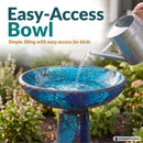 Crackled Glass Mosaic Bird Bath in deep ocean swirl shown outdoors in a garden as water is poured into the wide, shallow bowl, highlighting easy filling and access for birds.