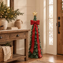 Green Christmas tree sculpture with a red bow and gold star displayed in a rustic entryway beside a console table and holiday greenery.