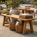 Sunnydaze Teak Trestle Bench in an upper class Mediterranean inspired backyard with blankets, figs, and a wicker basket of other decor underneath the product.